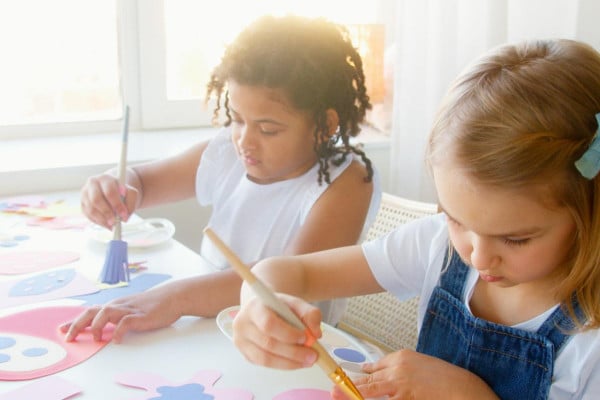 two young girls pretending to paint sat at a table