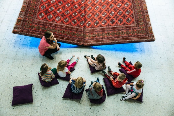 8 children sitting down on cushions with a teacher